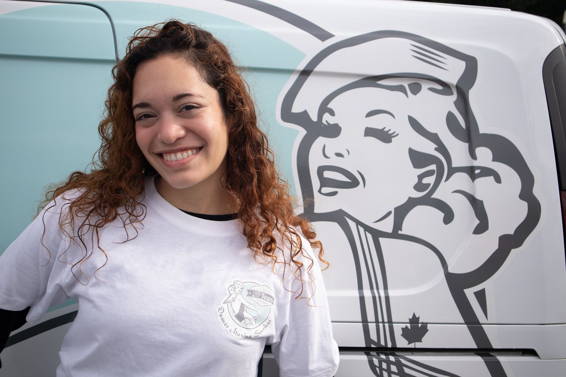 Woman smiling, standing by a van with a sailor girl graphic.