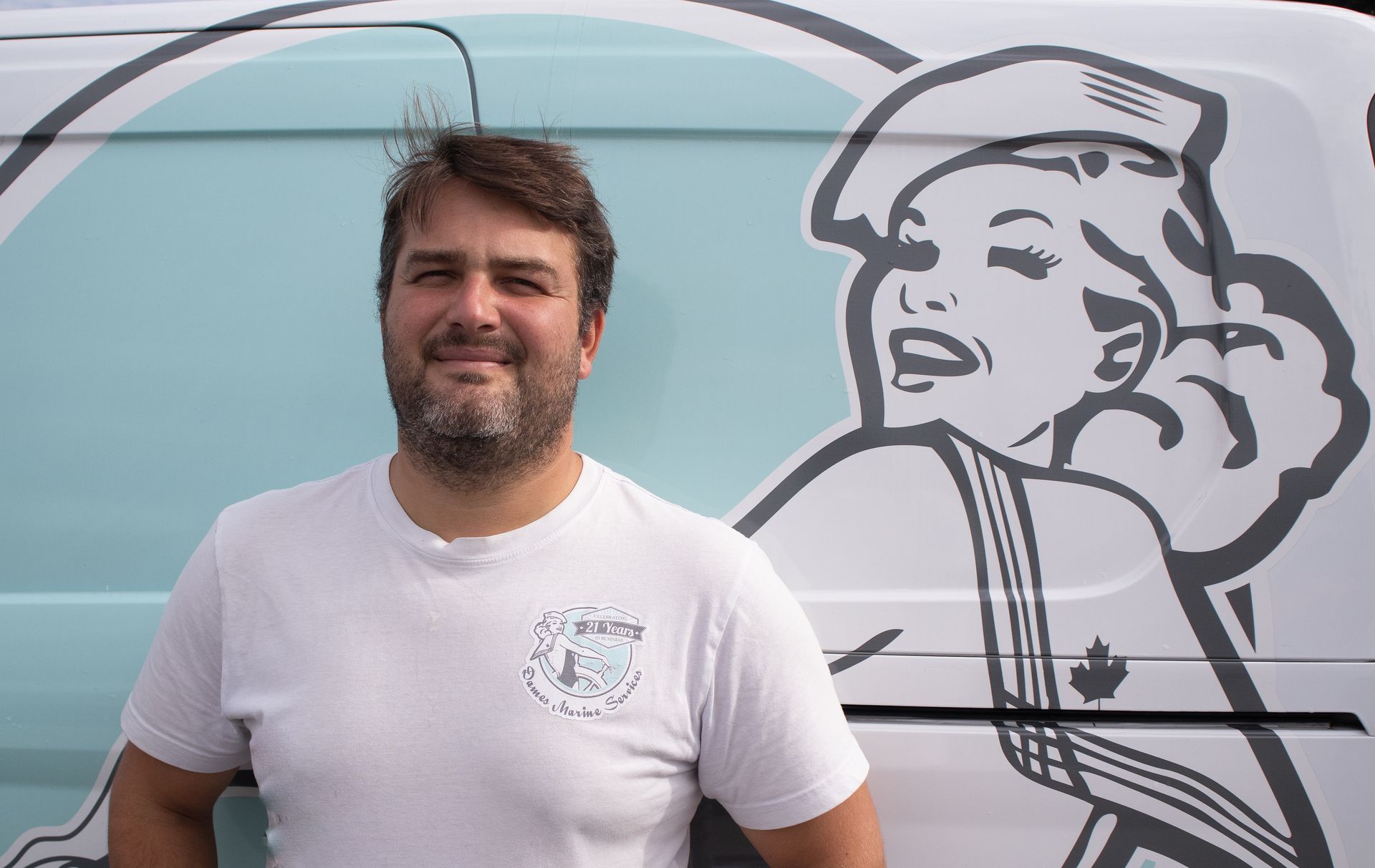 Man in white shirt smiling, standing in front of a van with a cartoon illustration of a woman on it.