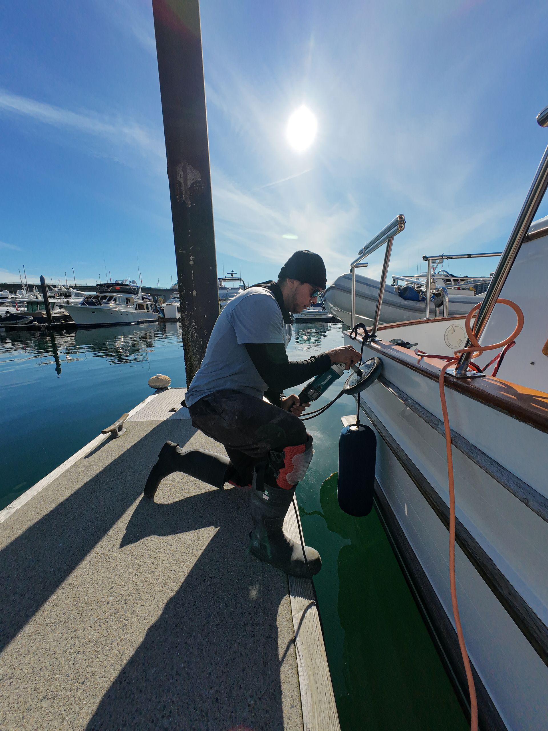 Man kneeling, working on a boat near a dock; sunny day.