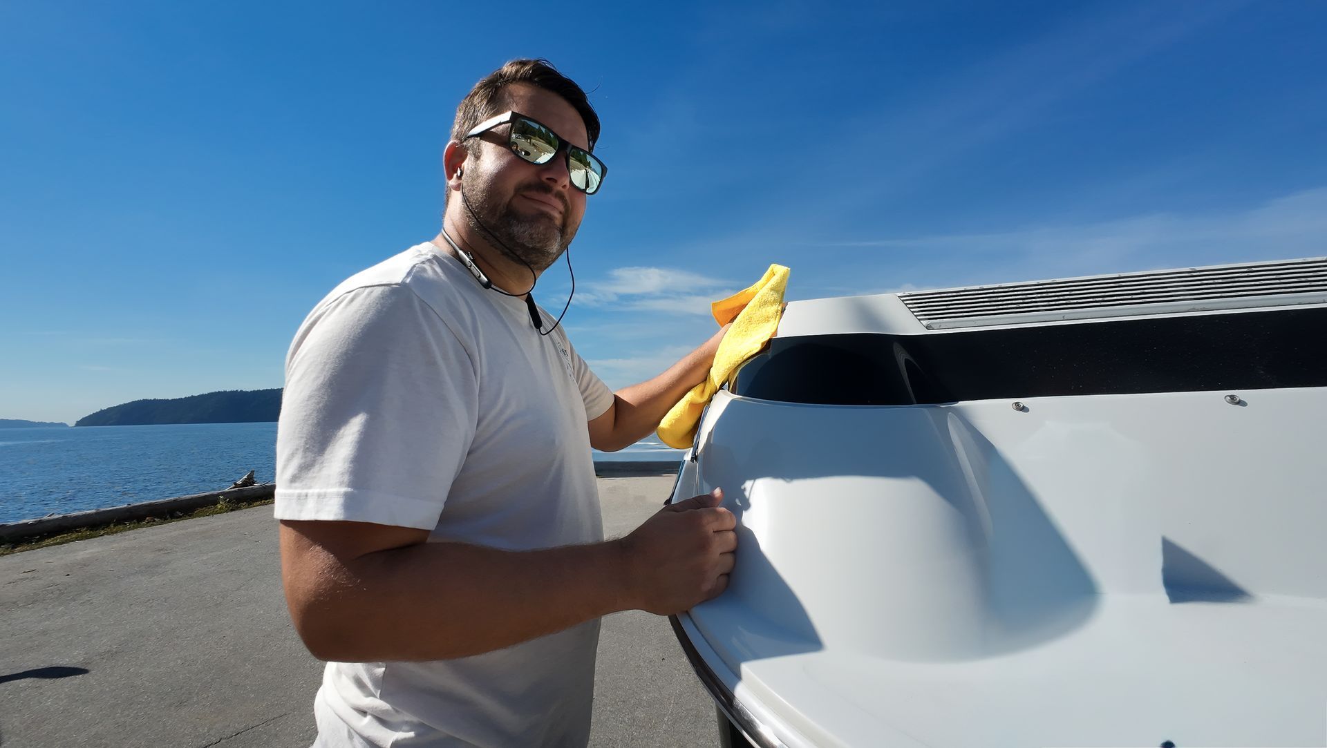 Man cleaning a white boat on a sunny day near water.