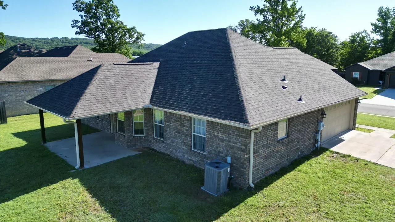 A wide, aerial view of a brick house featuring a sprawling hip roof covered in grey asphalt shingles