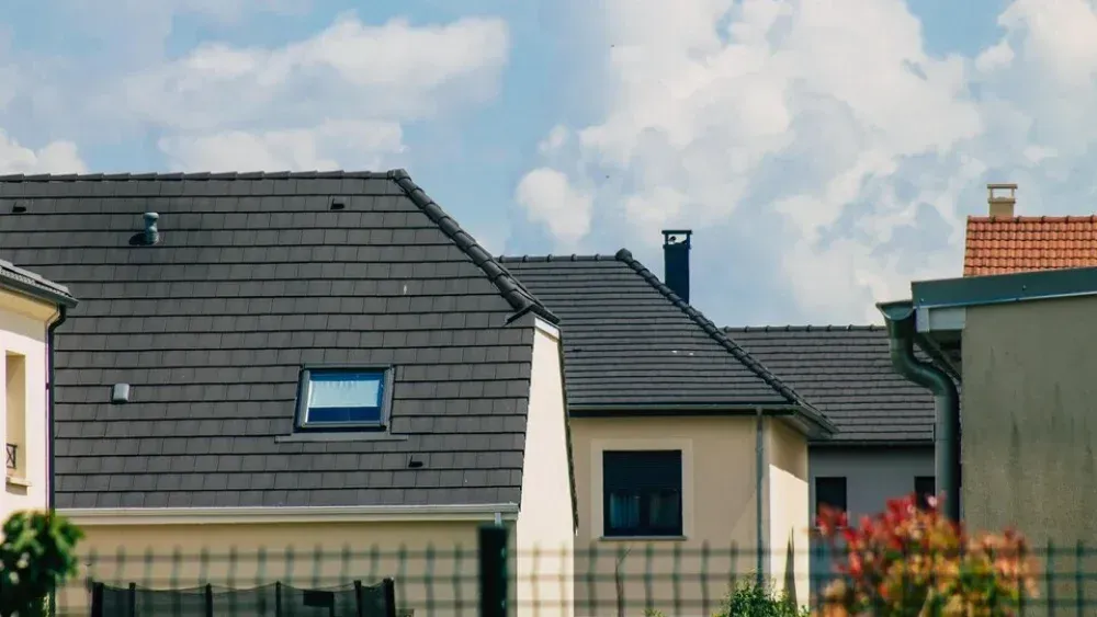 Several houses with dark grey shingle roofs and small skylights are seen under a bright, cloudy sky