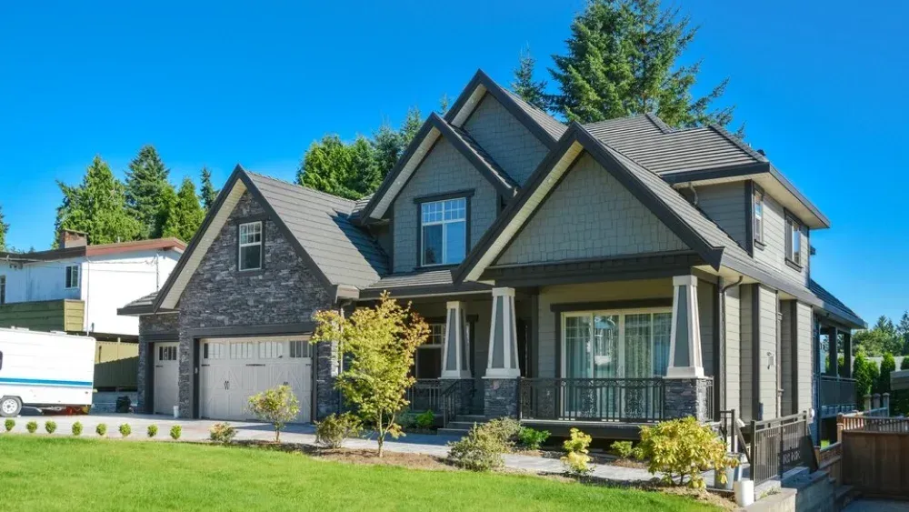 Gray and blue two-story house with green lawn, trees, and blue sky.
