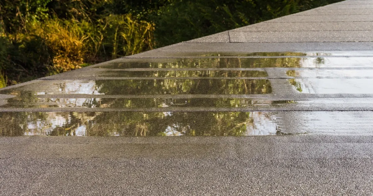 Puddles of standing water remain on a flat, gray gravel-surfaced roof after a recent rain