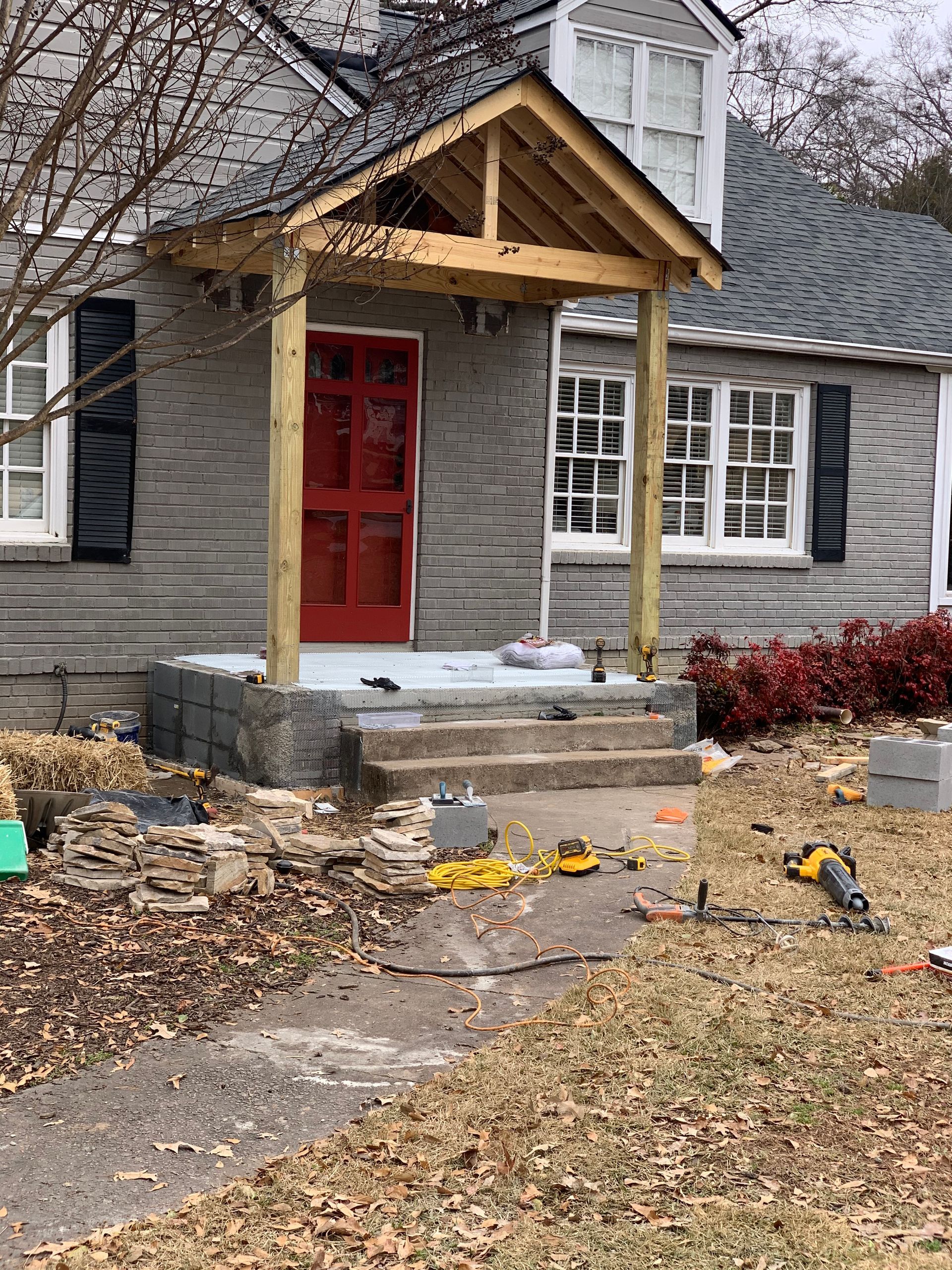 A gray house with a red door and a wooden porch