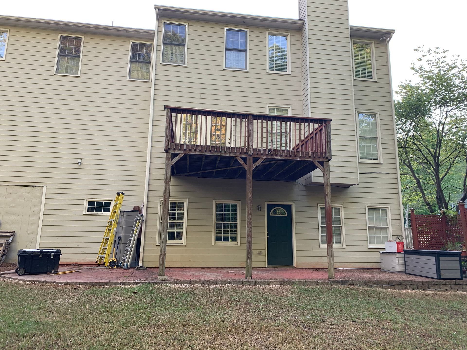 The back of a house with a deck and a ladder in front of it.