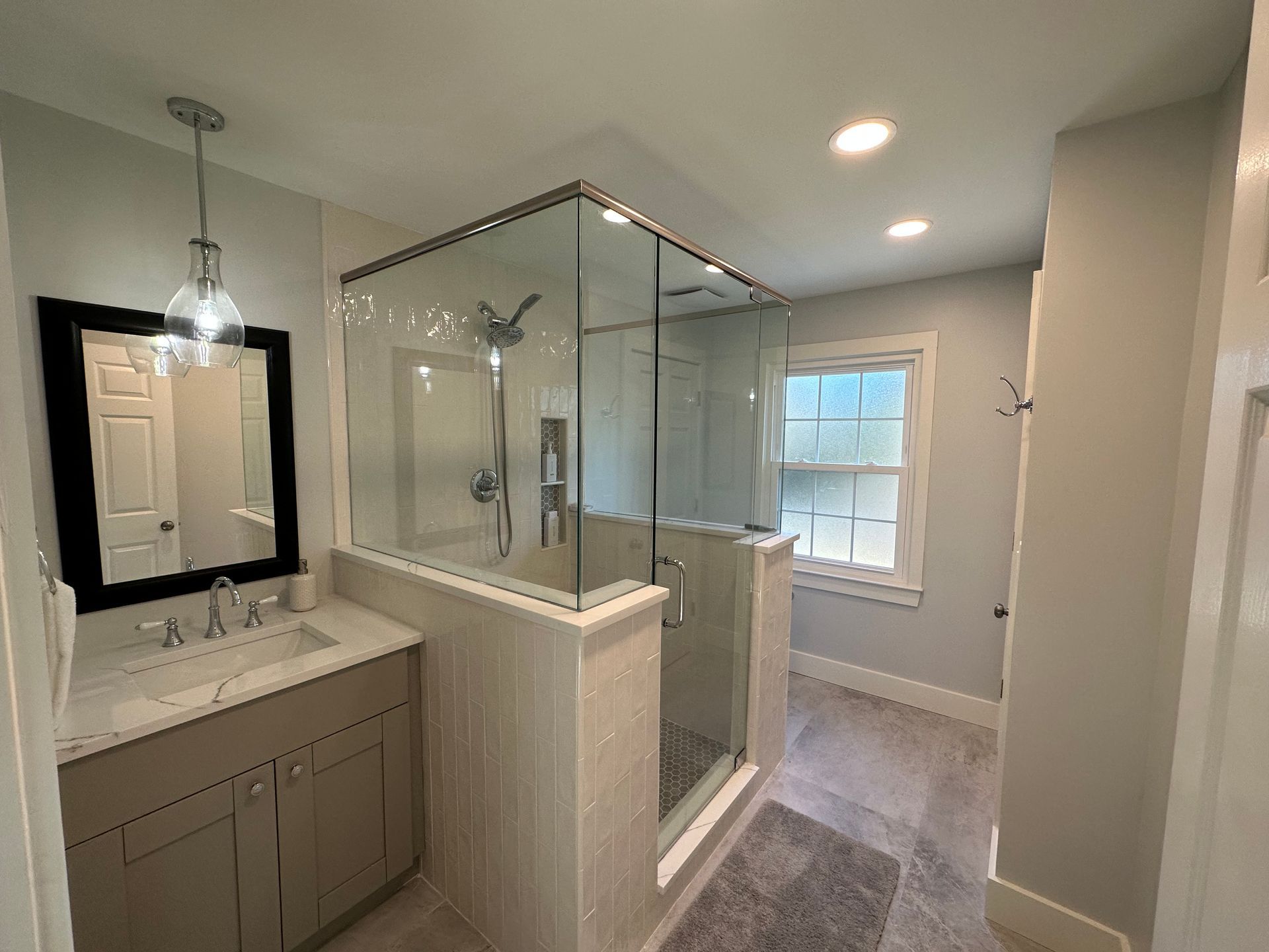 A bathroom with a walk in shower , sink , mirror and window.