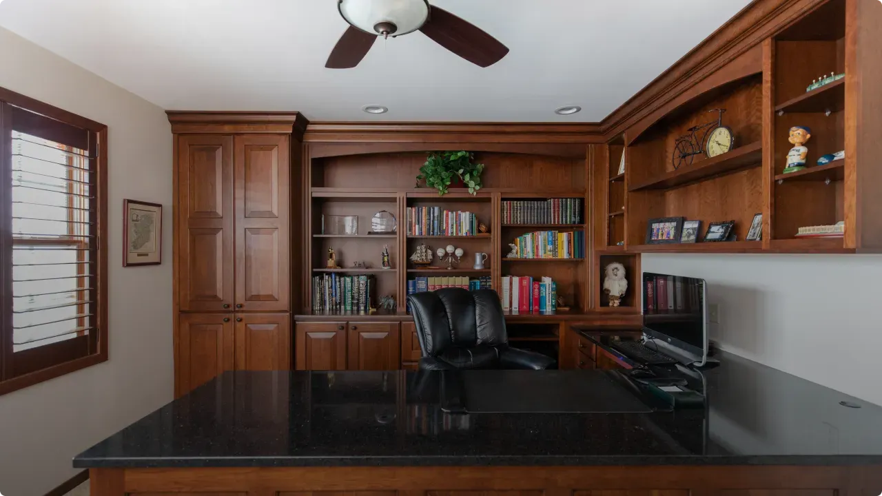 A home office with a black desk and a ceiling fan