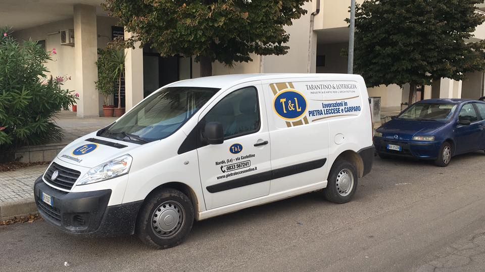 Un furgone bianco è parcheggiato sul ciglio della strada accanto a un'auto blu.