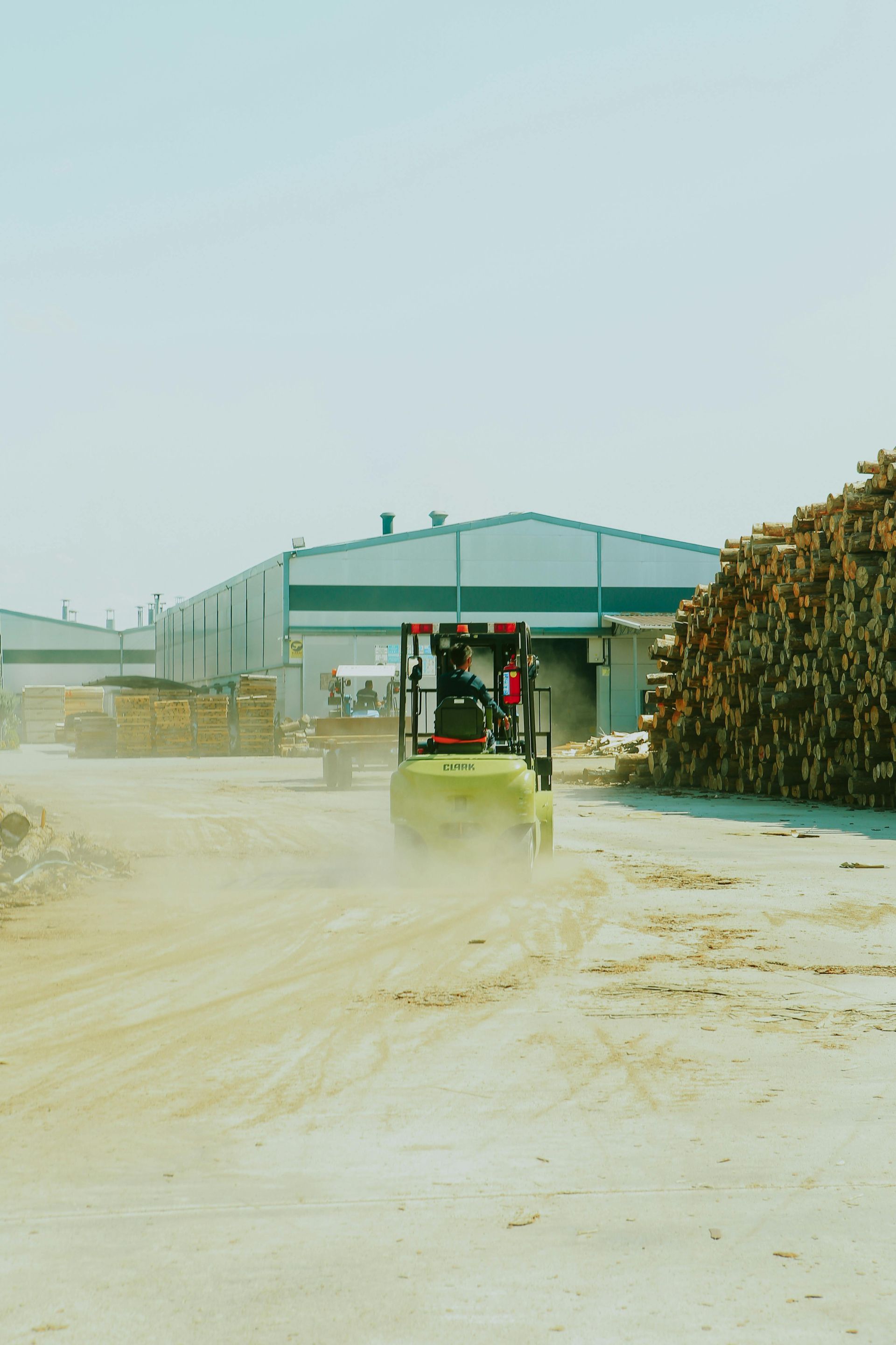 A forklift is driving down a dirt road in front of a building