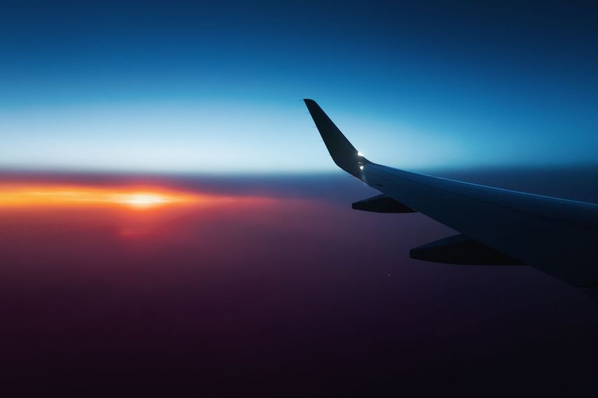 Airplane wing against a sunset, fiery orange and purple sky.