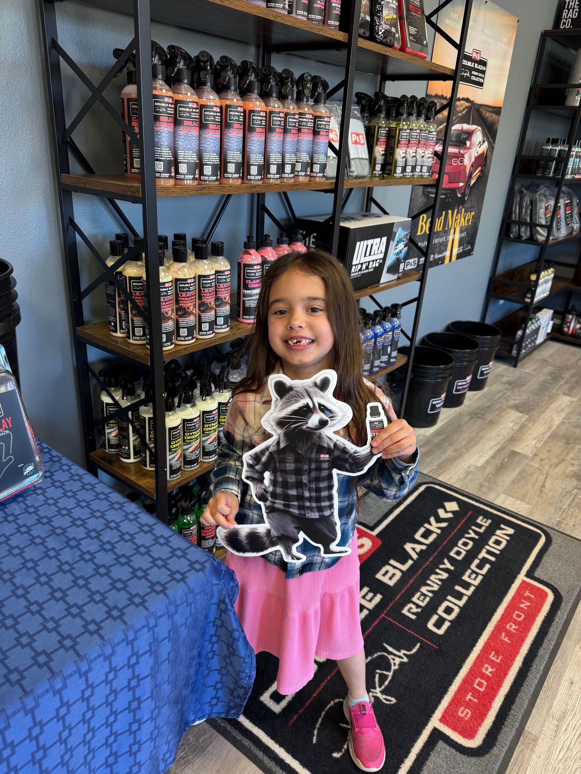A little girl is holding a raccoon sticker in a store.