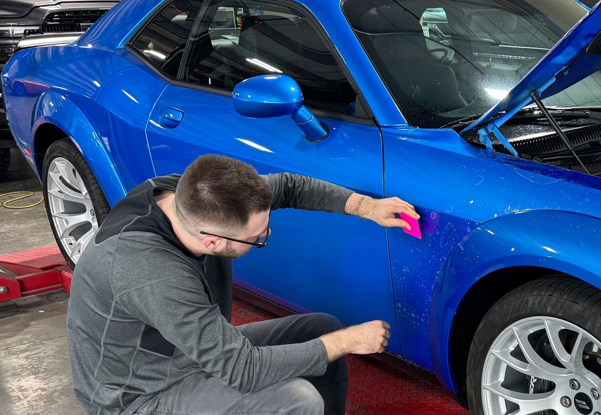 A man is kneeling down next to a blue car.