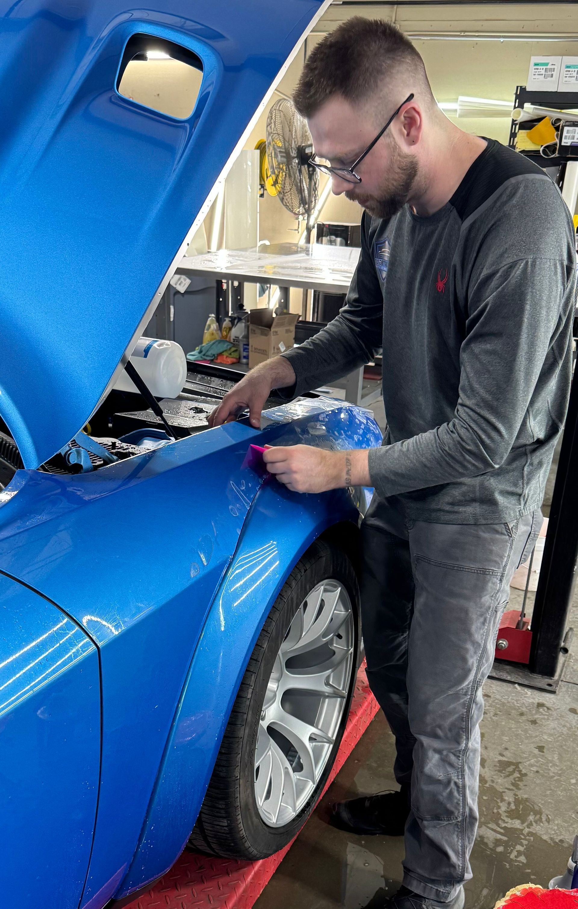 A man is standing next to a blue car with the hood open.
