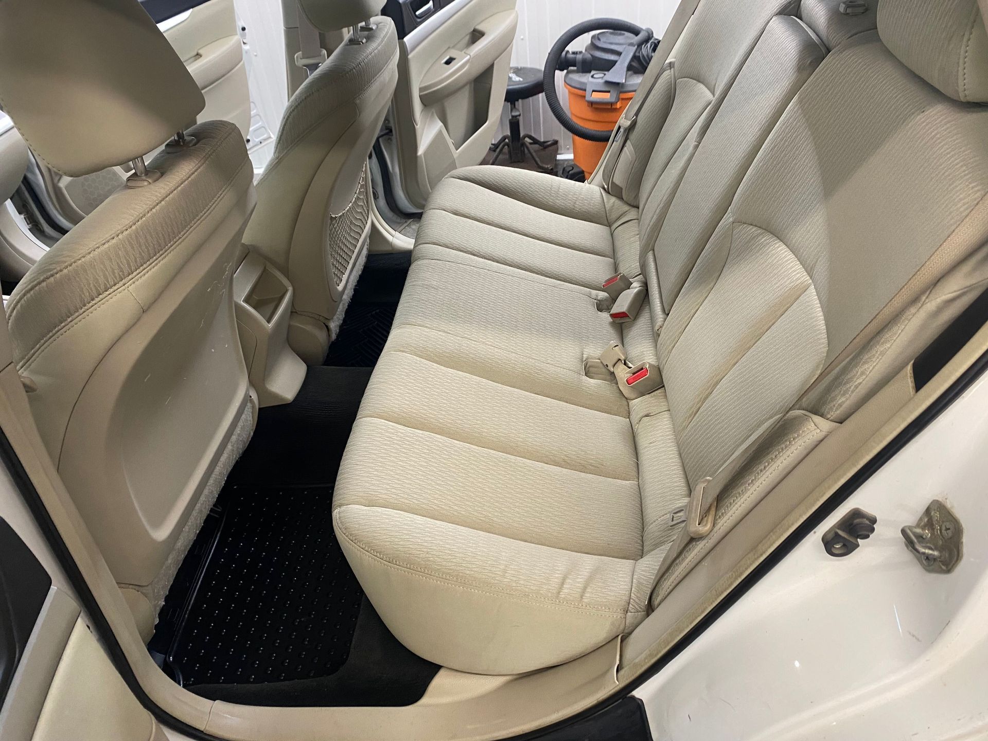 The back seat of a white car with a vacuum cleaner in the background.