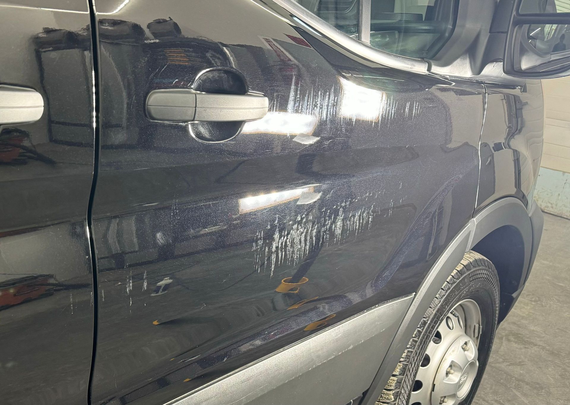 A black van with a scratch on the door is parked in a garage.