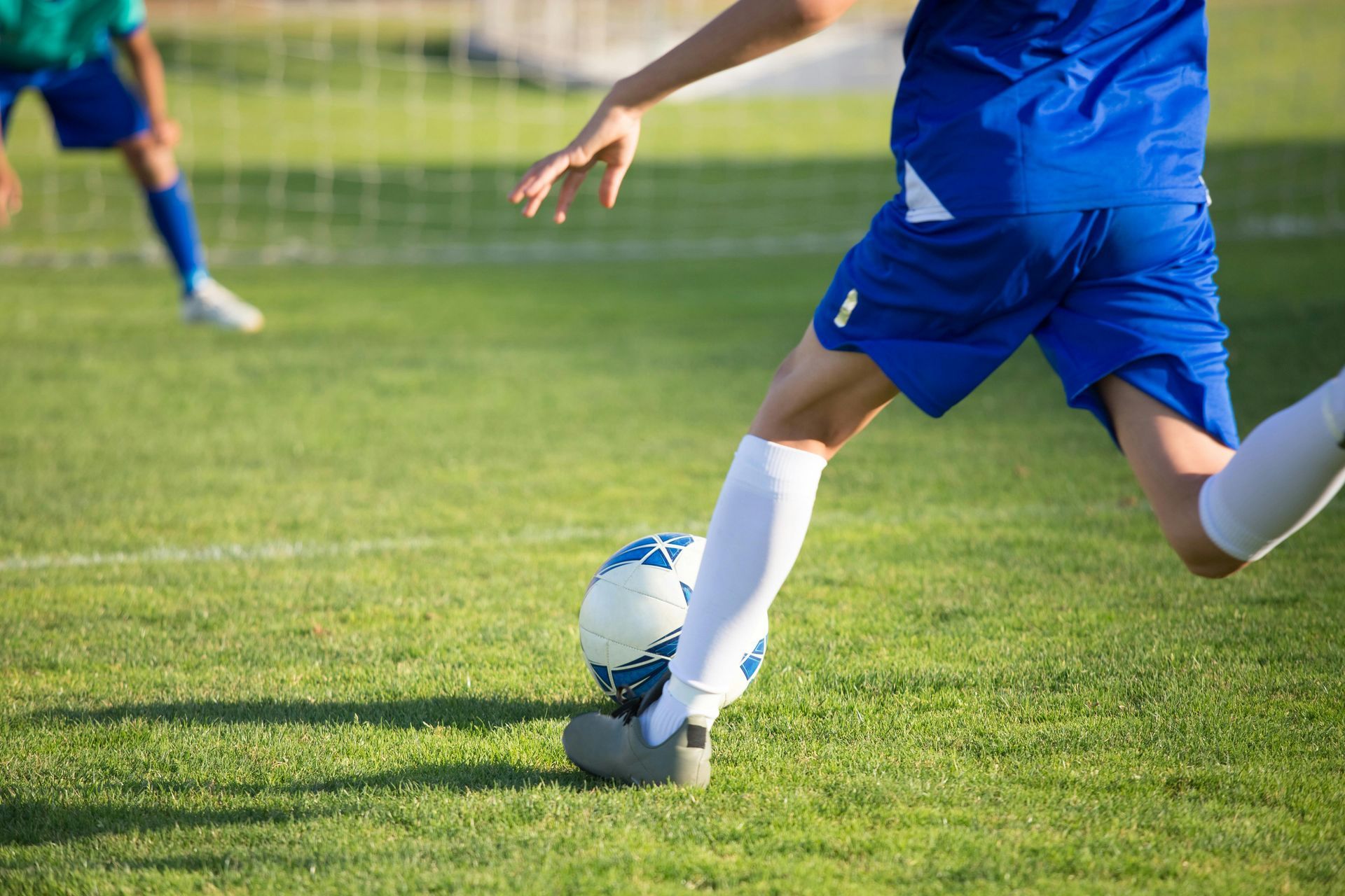 Soccer player in blue uniform kicking a soccer ball on a green field.