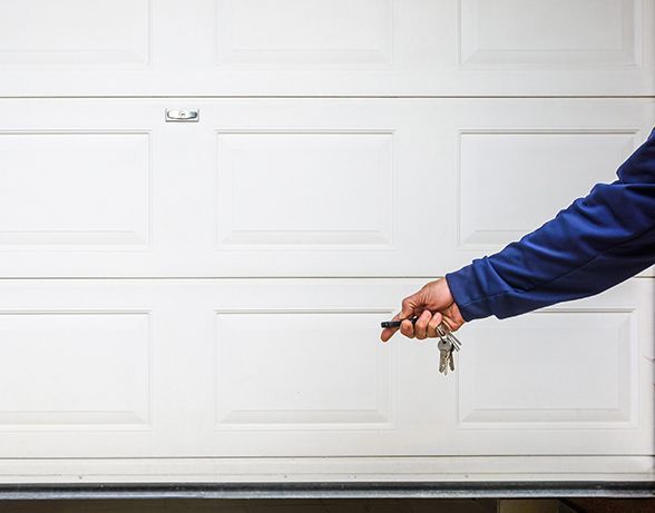 a person is holding a pair of keys in front of a garage door .