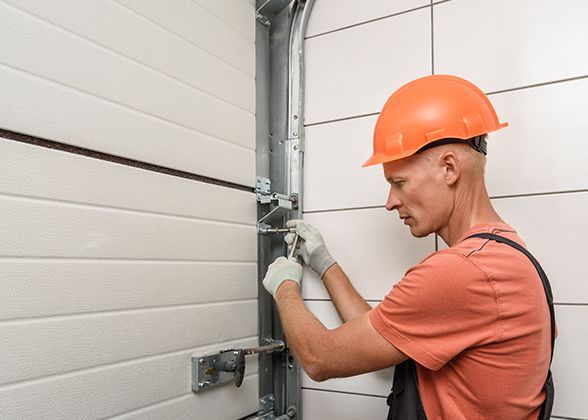 a man wearing a hard hat is working on a garage door .