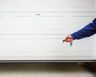 a person is holding a pair of keys in front of a garage door .