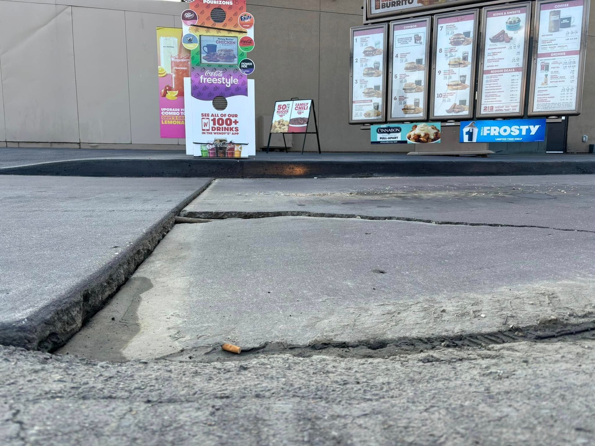A close-up view of a large, raised tripping hazard caused by uneven pavement in a fast-food drive-thru lane.
