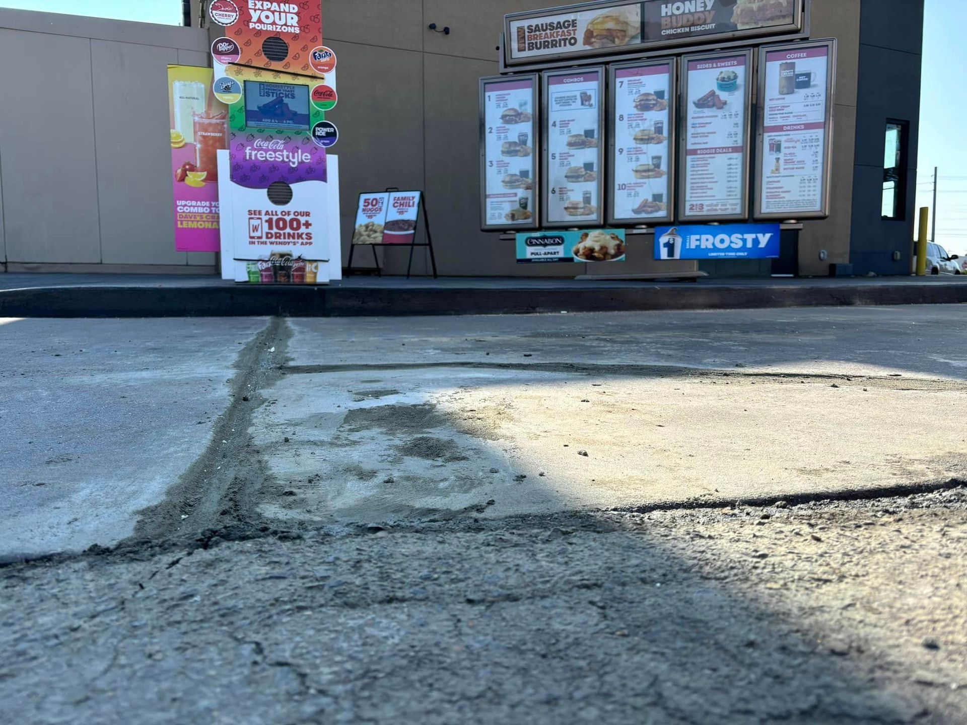 Close-up of cracked, uneven pavement in front of a Wendy’s drive-thru menu board.