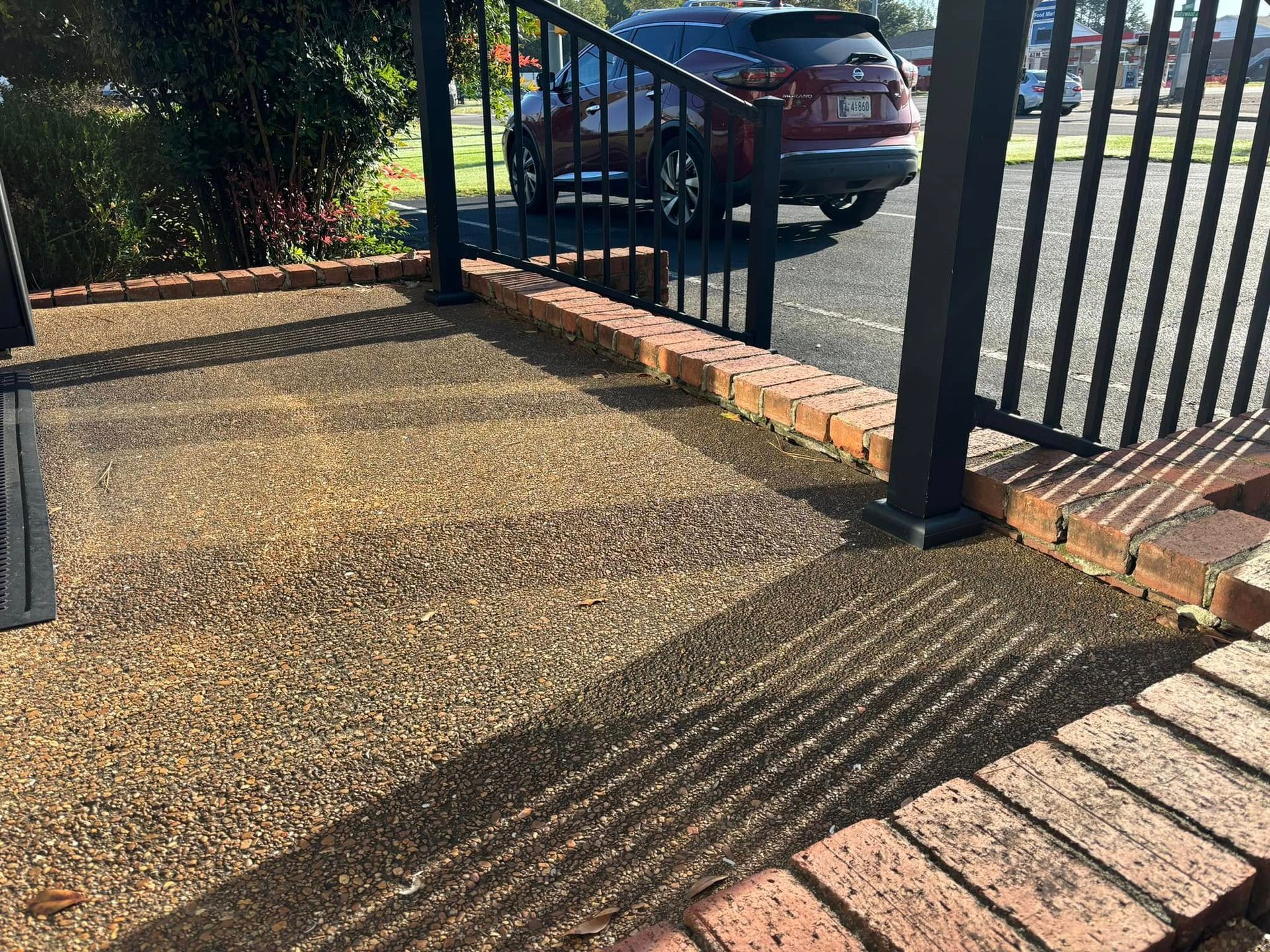 A textured patio floor made of small brown pebbles, bordered by red bricks and a black metal railing.