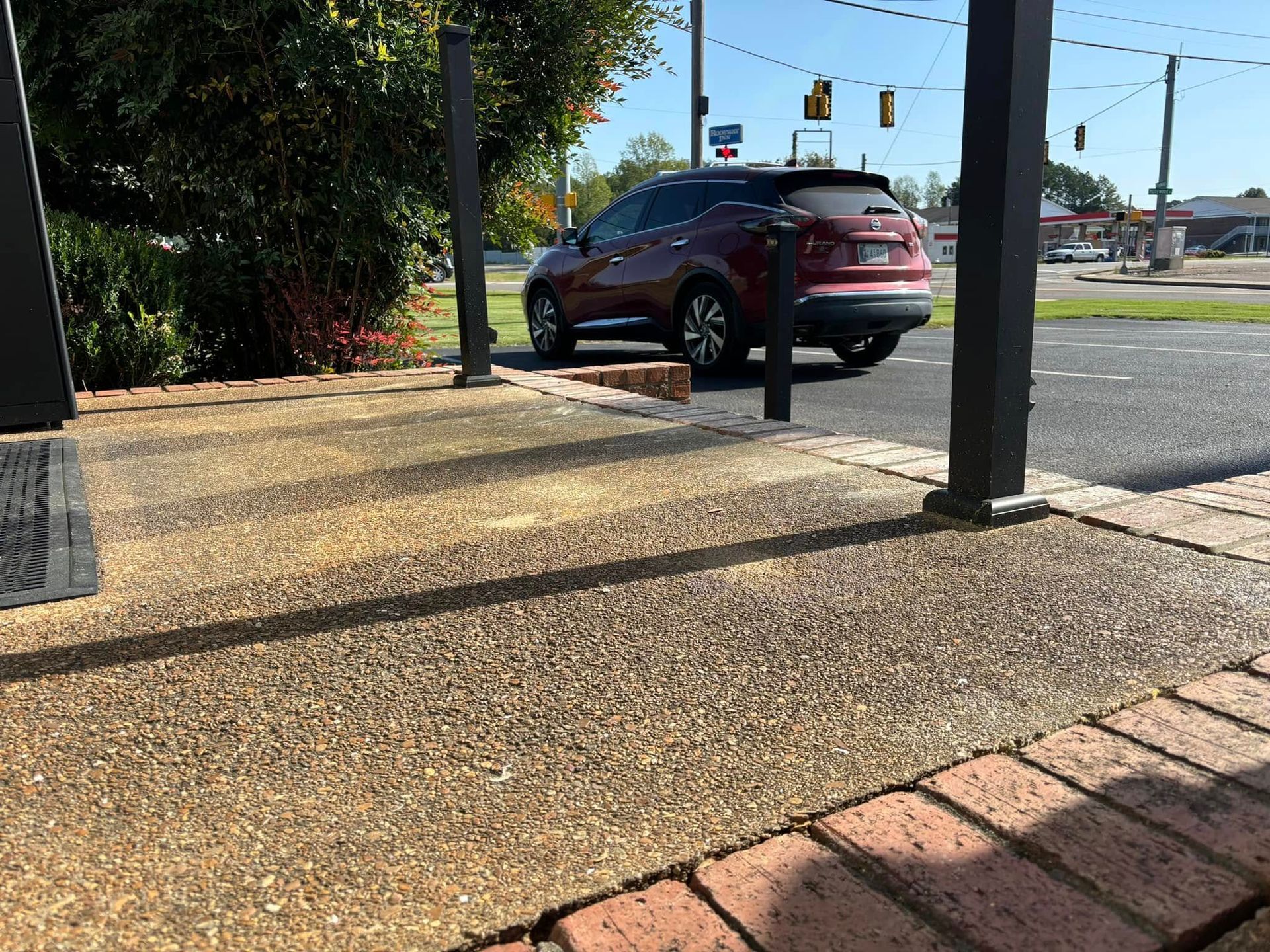 A view from a low-level, textured porch with dark posts overlooking a paved parking lot with a red SUV.