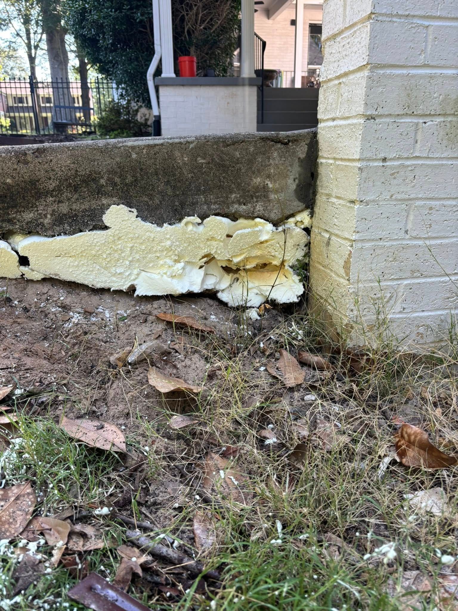 A concrete porch edge with exposed yellow spray foam insulation where it meets a brick foundation wall.