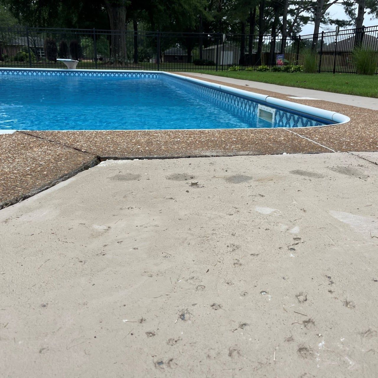 A concrete patio surface leading to the edge of a swimming pool on a sunny day.