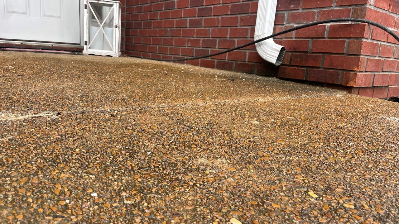 A view of an exposed aggregate concrete porch with a red brick wall, a white downspout, and a lantern near the door.