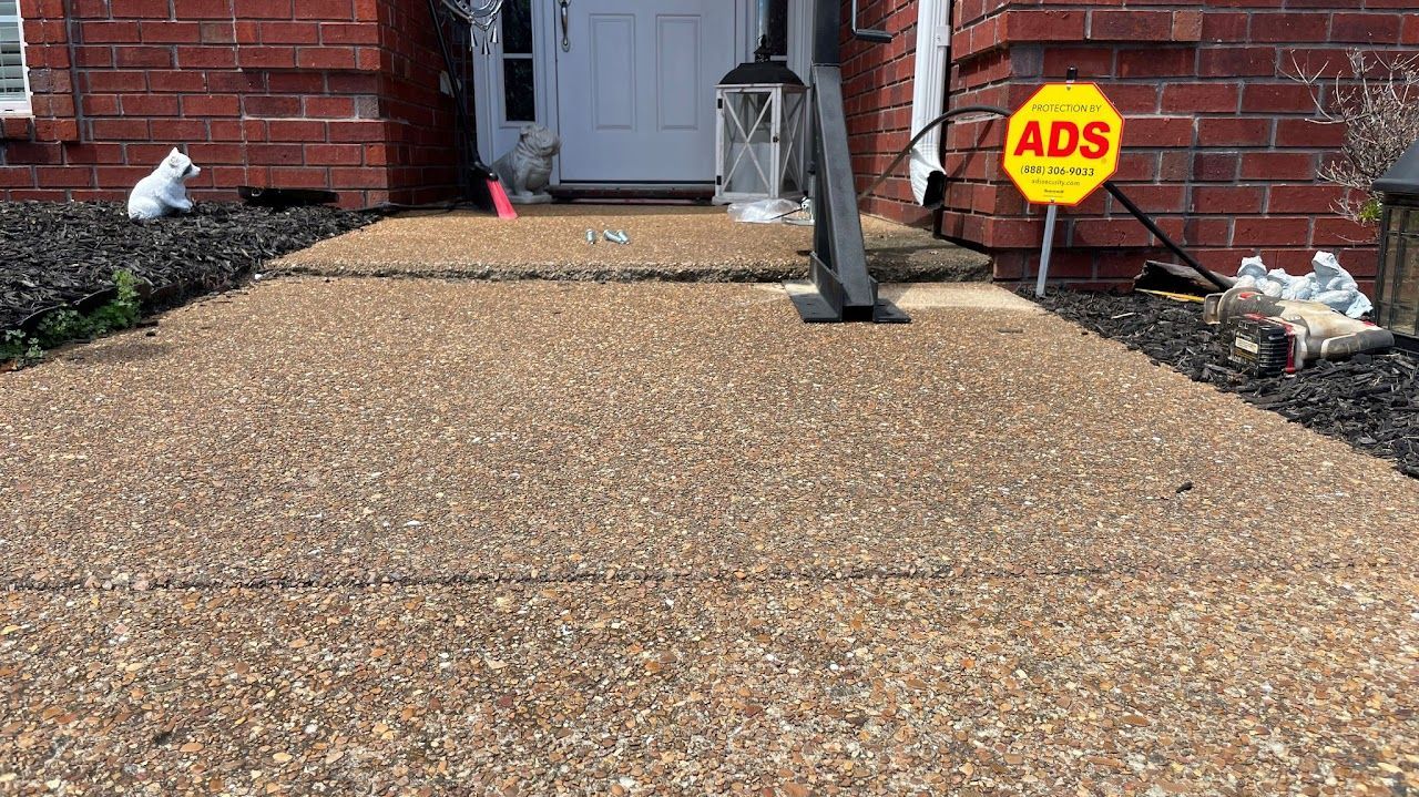 A slightly uneven concrete walkway leads to a front door with an ADS security sign on the brick wall nearby.