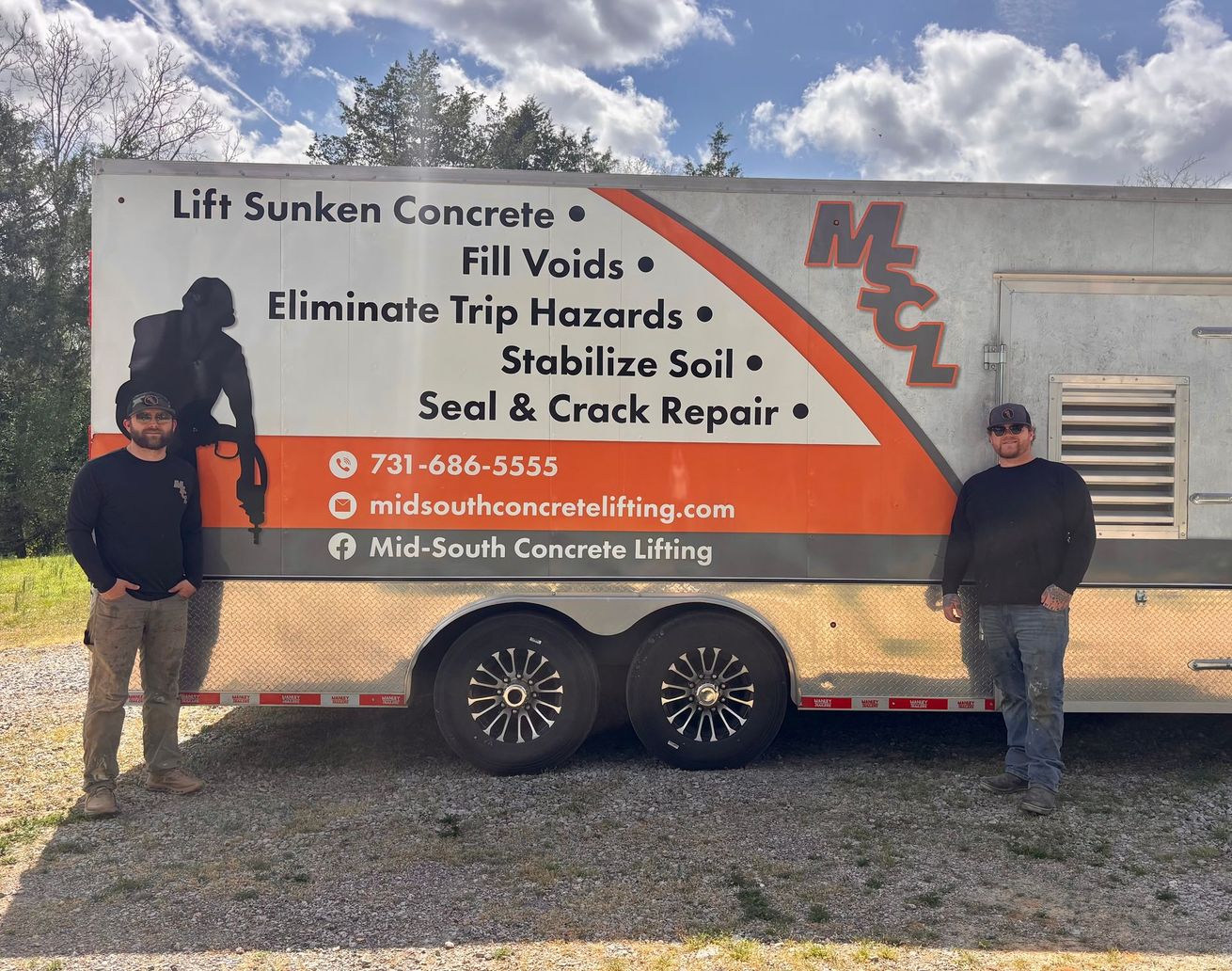 Three construction workers in hard hats and safety vests consult building plans spread out on the ground.