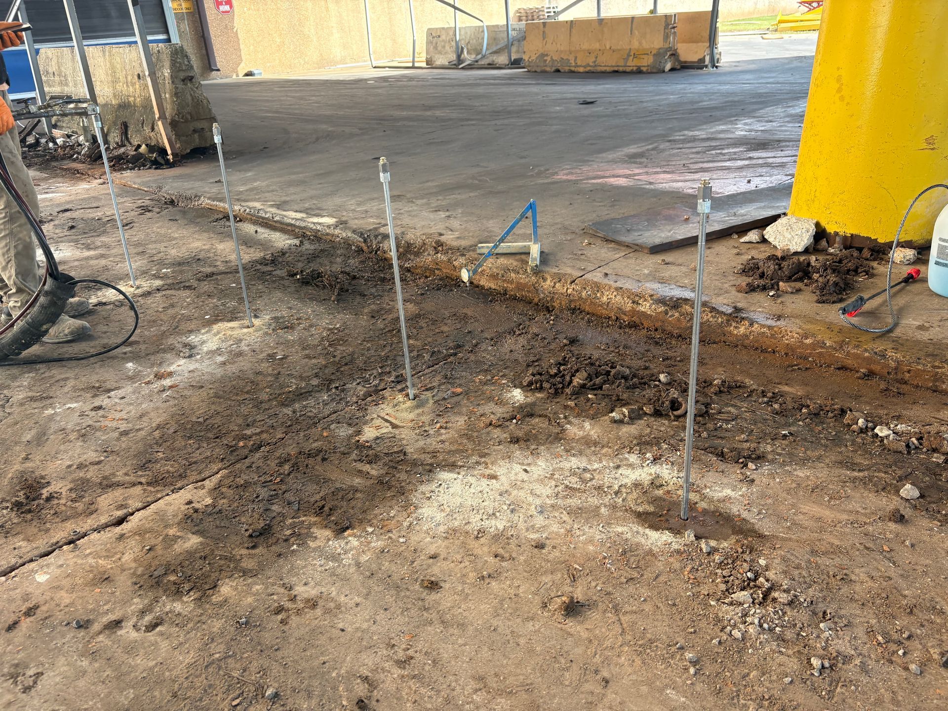A worker in a blue uniform and gloves uses a yellow spirit level on a paved surface at a construction site.