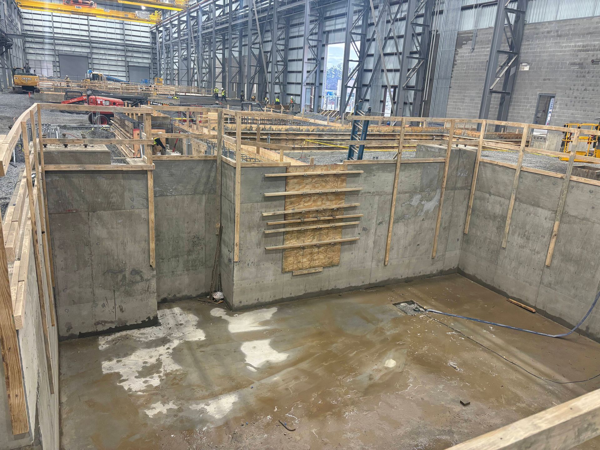 A construction worker in a yellow hard hat and grey uniform uses a spirit level on a concrete curb at a building site.
