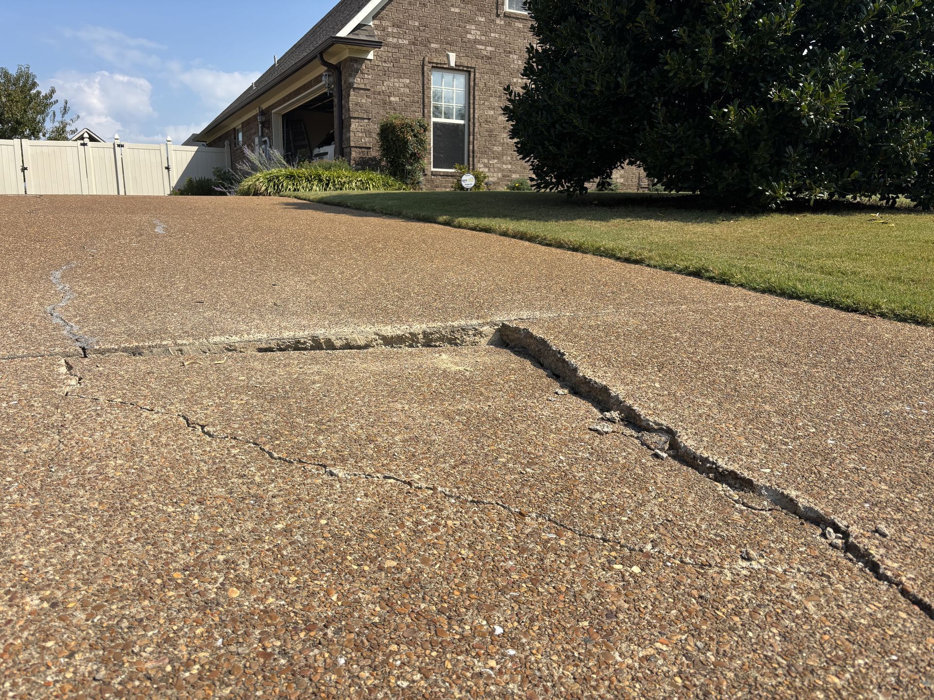 A concrete patio path leads to a garden bed with red brick accents, chairs, and a small building in the background.