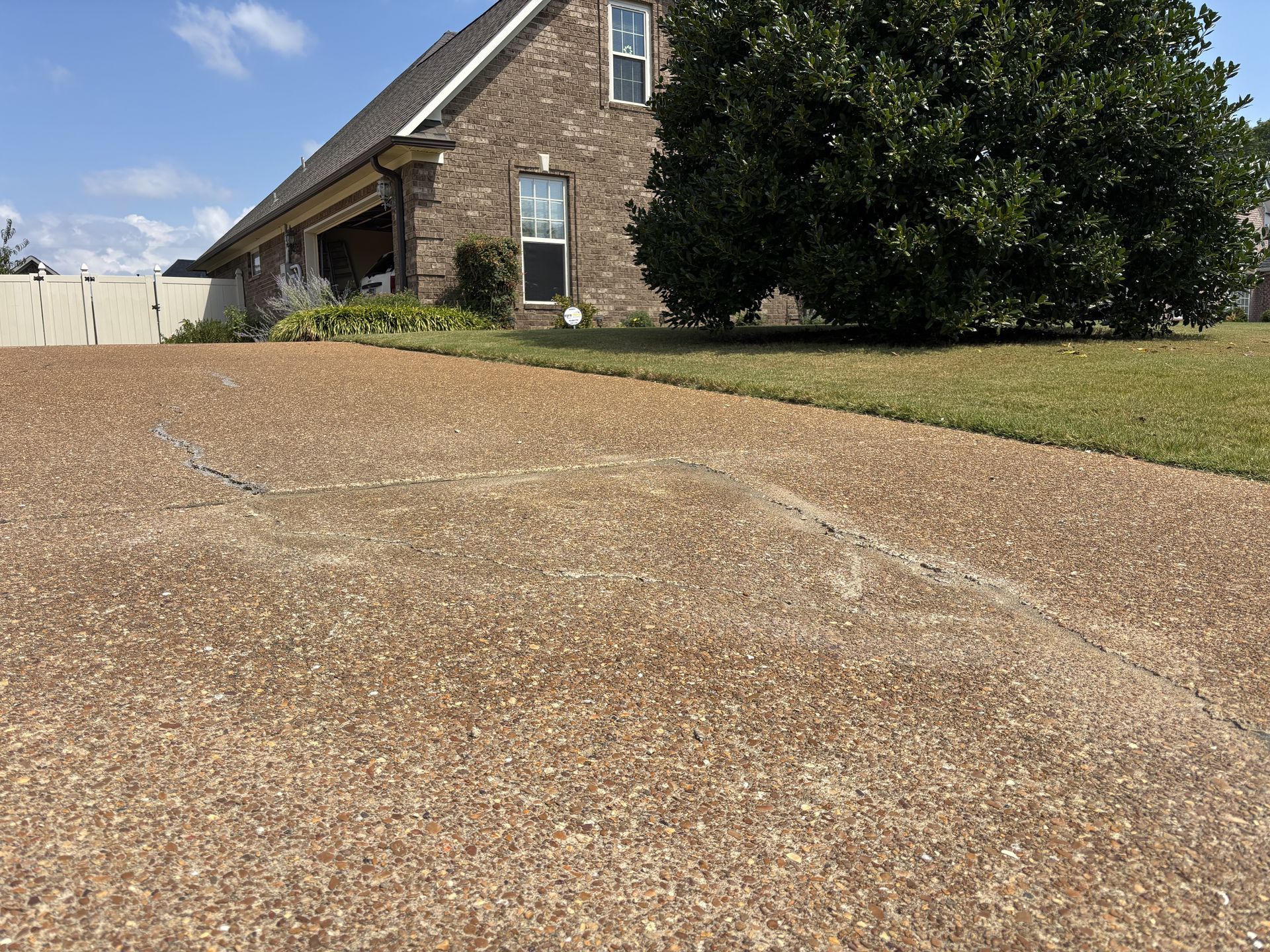 A concrete patio edge leading to a backyard with a small structure featuring a purple roof, trees, and fencing.