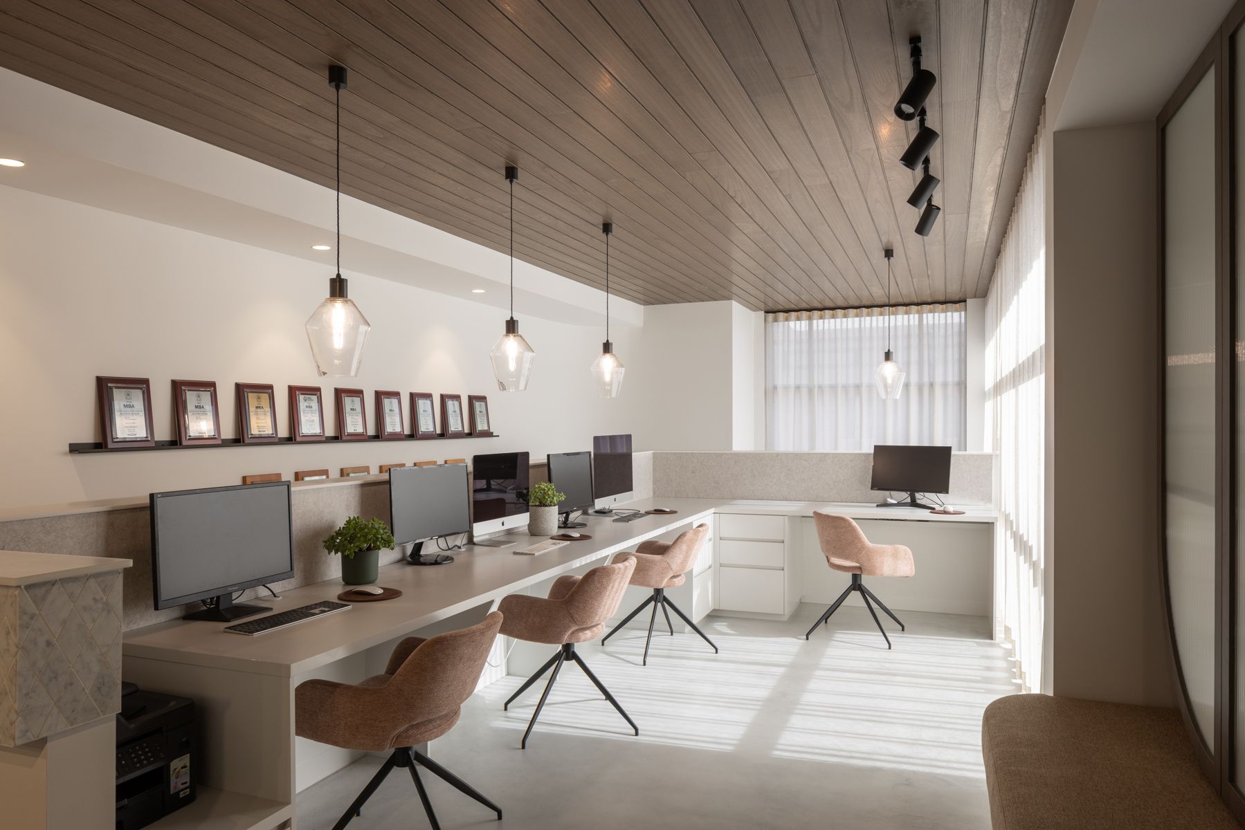 Modern office with computers, pink chairs, and decorative lighting. — Goode By Design in Unanderra, NSW