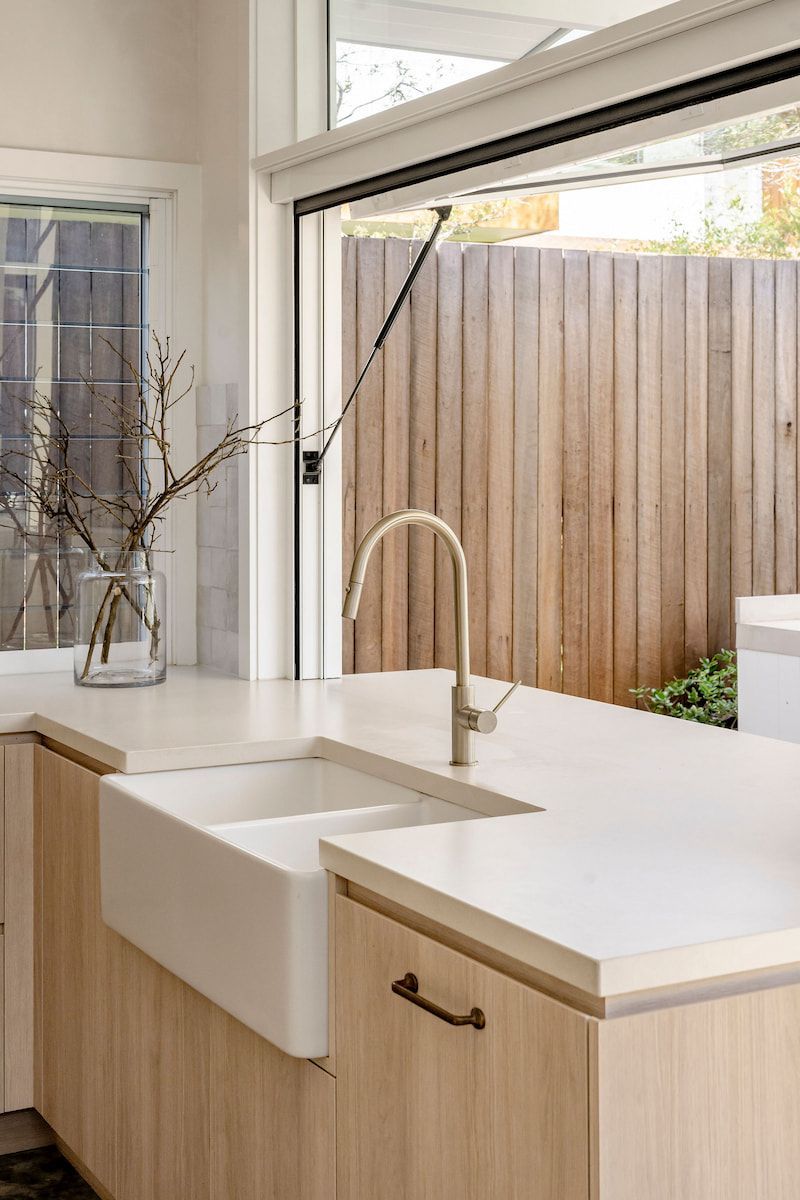 Kitchen Island With White Sink, Faucet, and Light Wood Cabinets, Beside an Open Window — Goode By Design in Unanderra, NSW