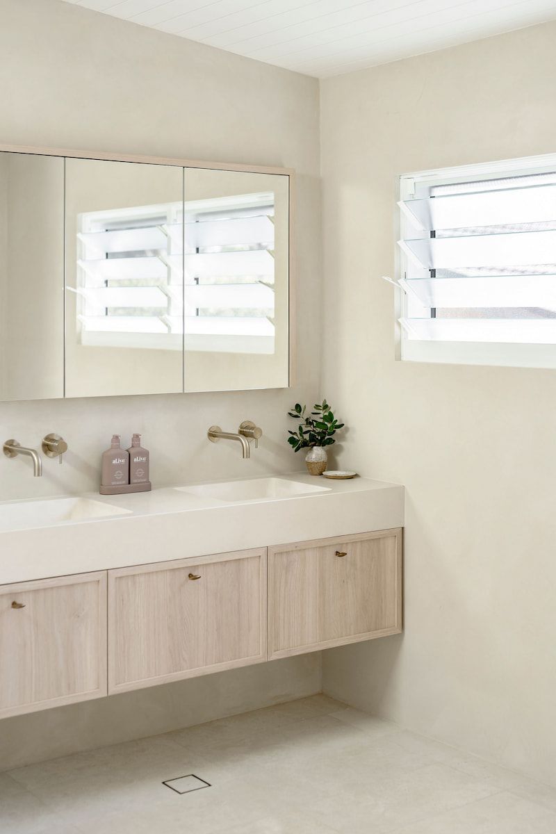 Neutral-toned Modern Bathroom With a Floating Vanity, Double Sinks, Mirror, and a Window With Louvers — Goode By Design in Unanderra, NSW