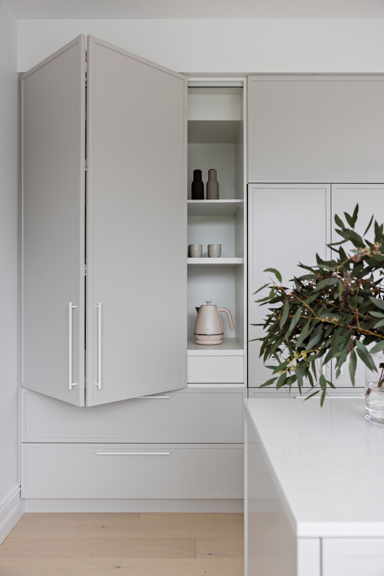 Gray kitchen cabinet with open door, showing interior shelves holding glassware and a kettle. — Goode By Design in Unanderra, NSW