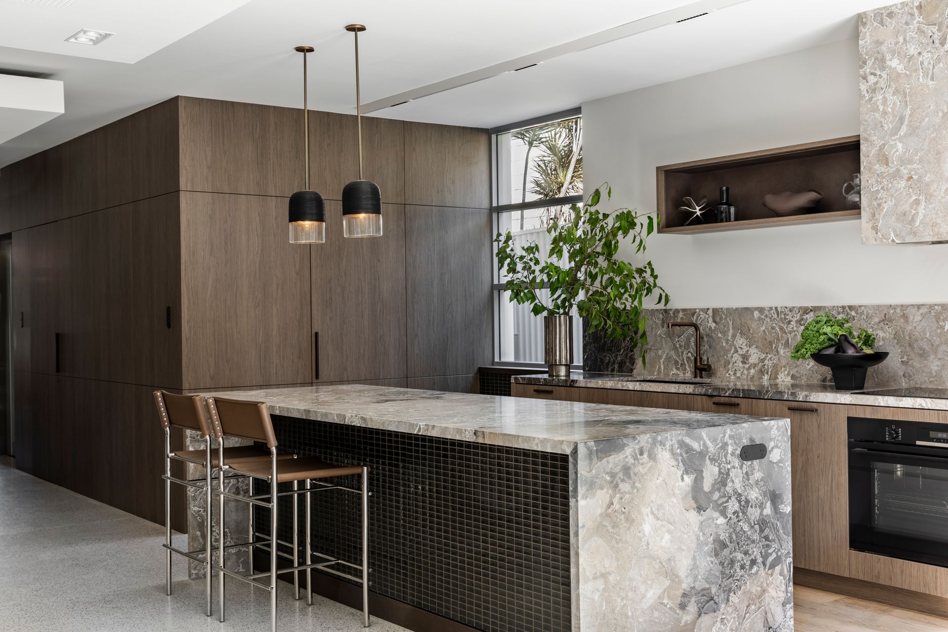 Modern kitchen with dark wood cabinets, marble island, pendant lights, and built-in appliances