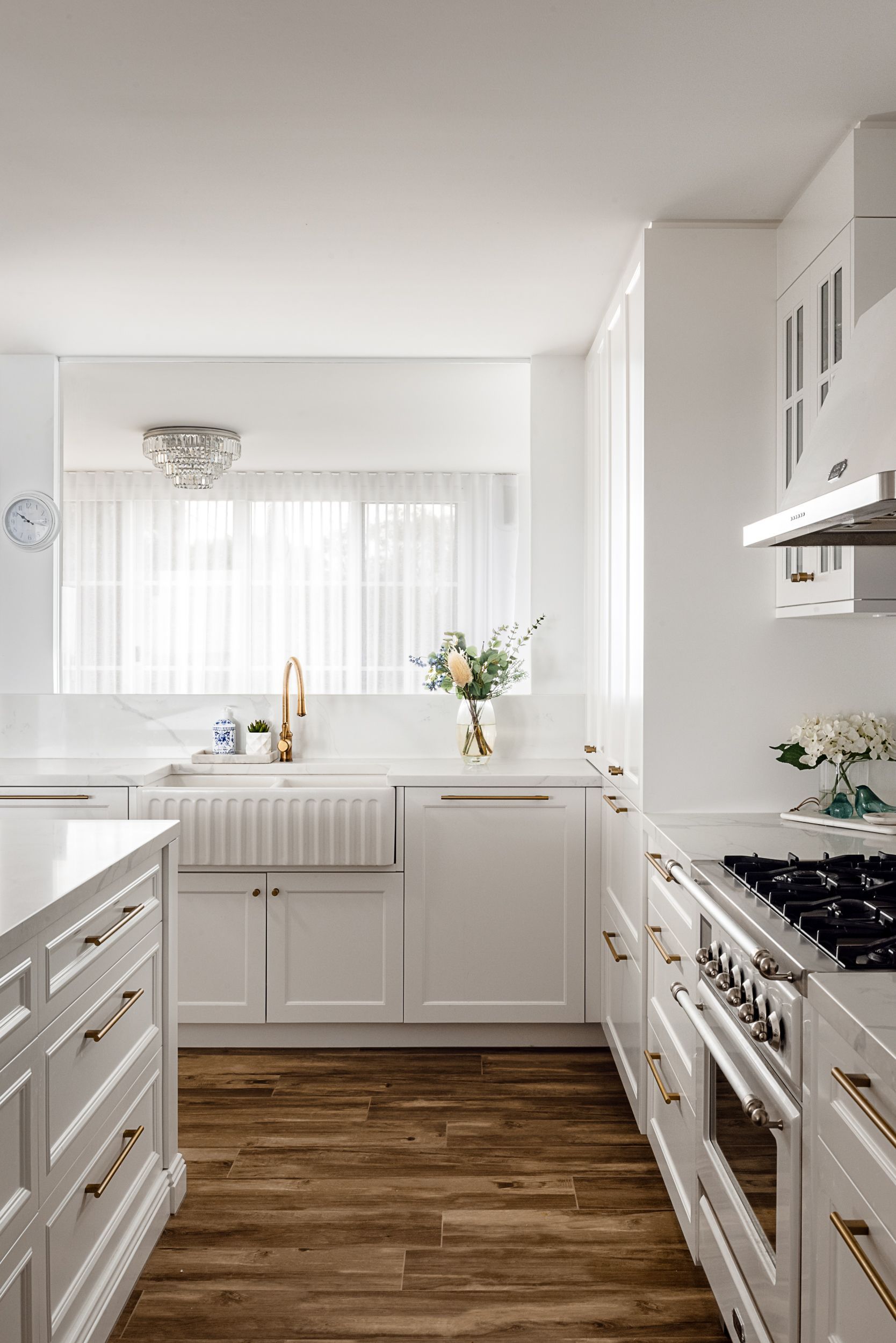 White kitchen with wood floor, island, and stainless steel appliances. — Goode By Design in Unanderra, NSW