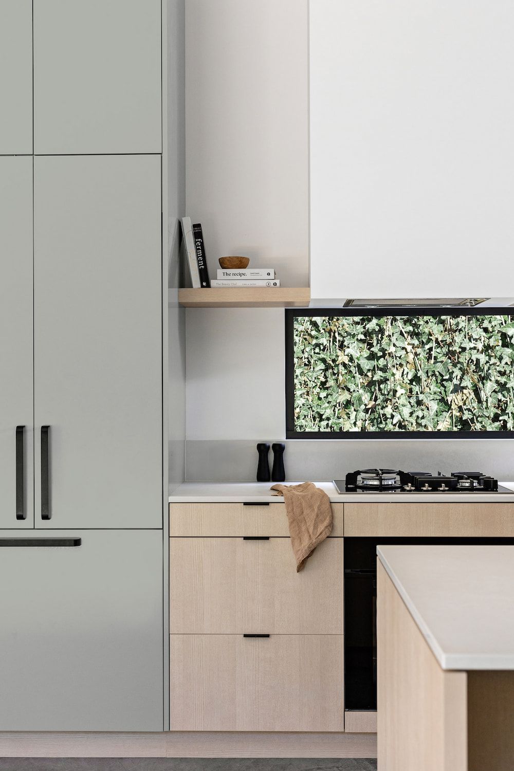 Modern kitchen with light green cabinetry, wooden accents, and a TV above the stove. — Goode By Design in Southern Highlands, NSW