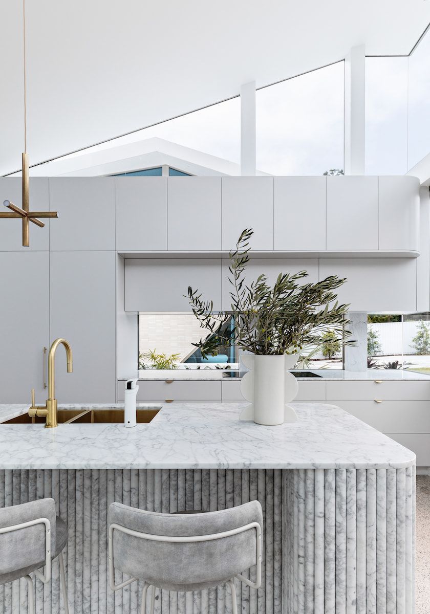 Modern kitchen with marble island, gold fixtures, white cabinets, and plants. — Goode By Design in Sydney Joinery, NSW