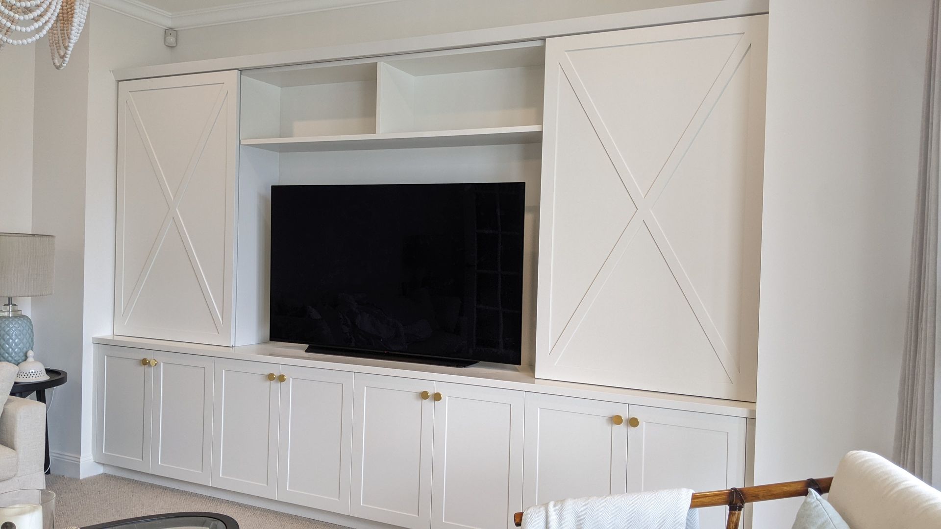 White built-in entertainment center with TV, shelves, and cabinet doors. — Goode By Design in Unanderra, NSW