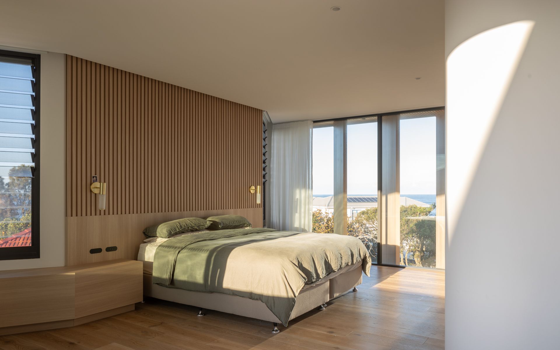 Bedroom with wooden paneling, a bed with green bedding, and large windows with ocean view.