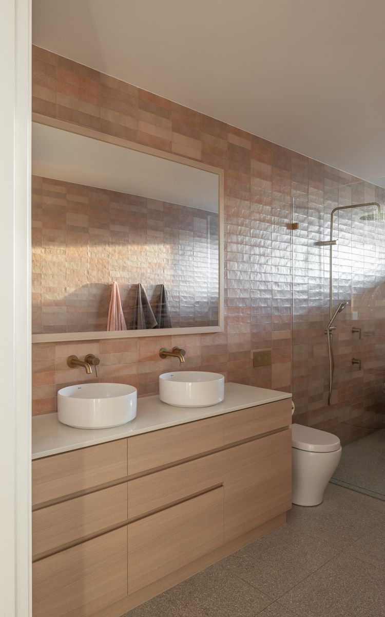 Bathroom with double sinks, light wood cabinetry, and tiled walls, neutral color palette.