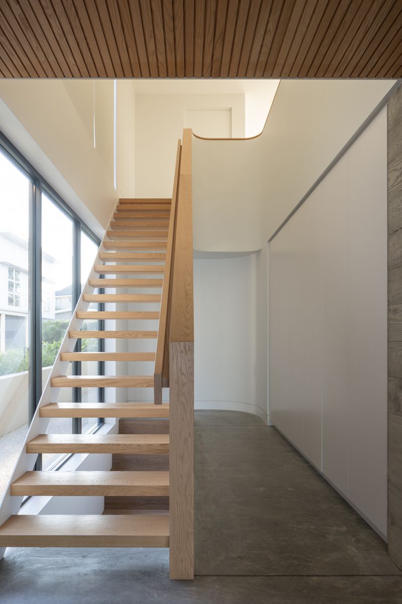 Wooden staircase in modern white hallway. Sunlight streams in from a large window.