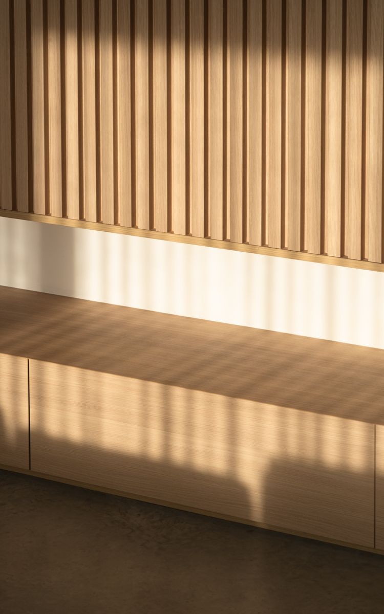 Wooden slatted wall with a bench, lit by sunlight creating striped shadows.